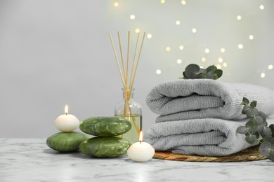 Spa composition. Towels, stones, reed air freshener and burning candles on white marble table