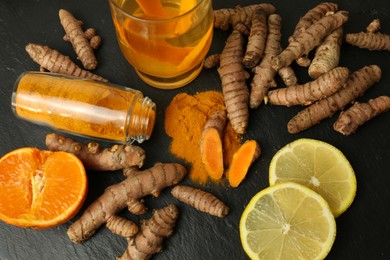 Photo of Turmeric roots, powder, sliced lemon and cup of tasty tea on black textured table, flat lay