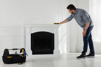 Photo of Man using construction level for installing electric fireplace near white wall in room