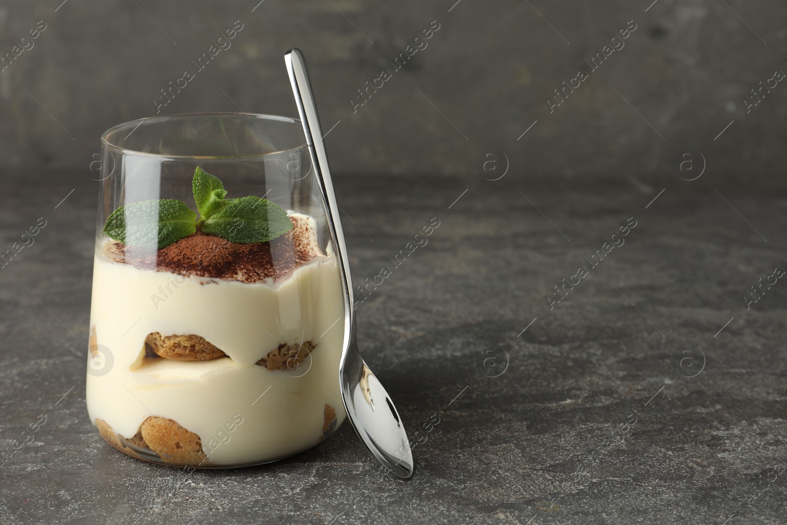 Photo of Delicious tiramisu with mint in glass on grey table. Space for text