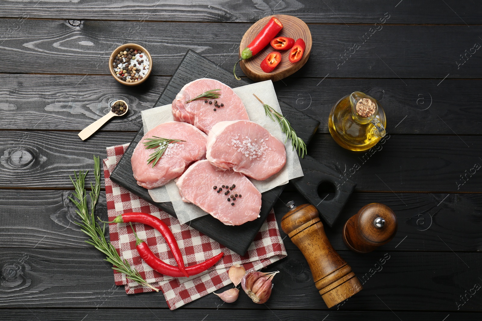 Photo of Pieces of raw pork meat, chili pepper, spices and oil on black wooden table, flat lay
