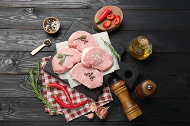 Pieces of raw pork meat, chili pepper, spices and oil on black wooden table, flat lay