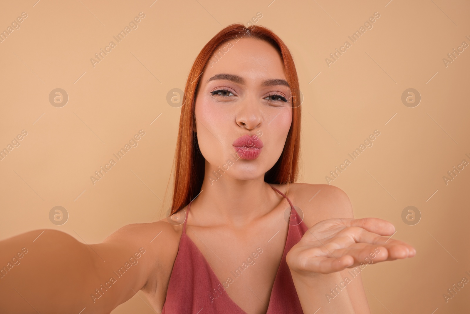 Photo of Beautiful woman taking selfie and blowing kiss on beige background