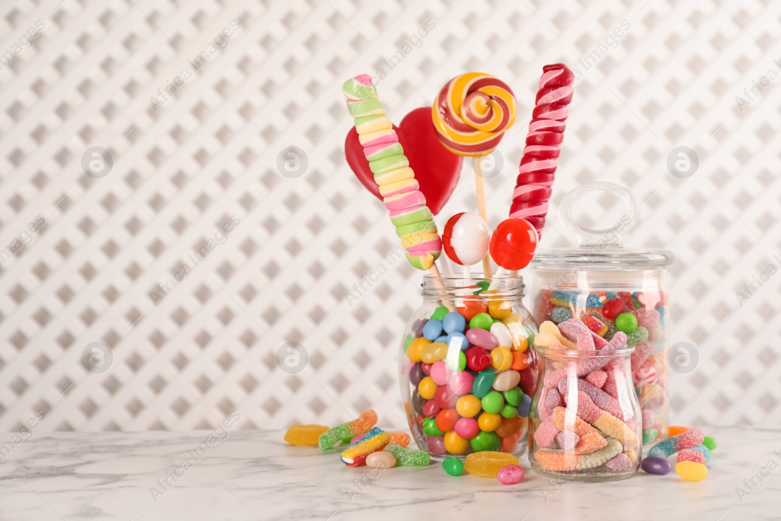Photo of Jars with different delicious candies on white marble table, space for text