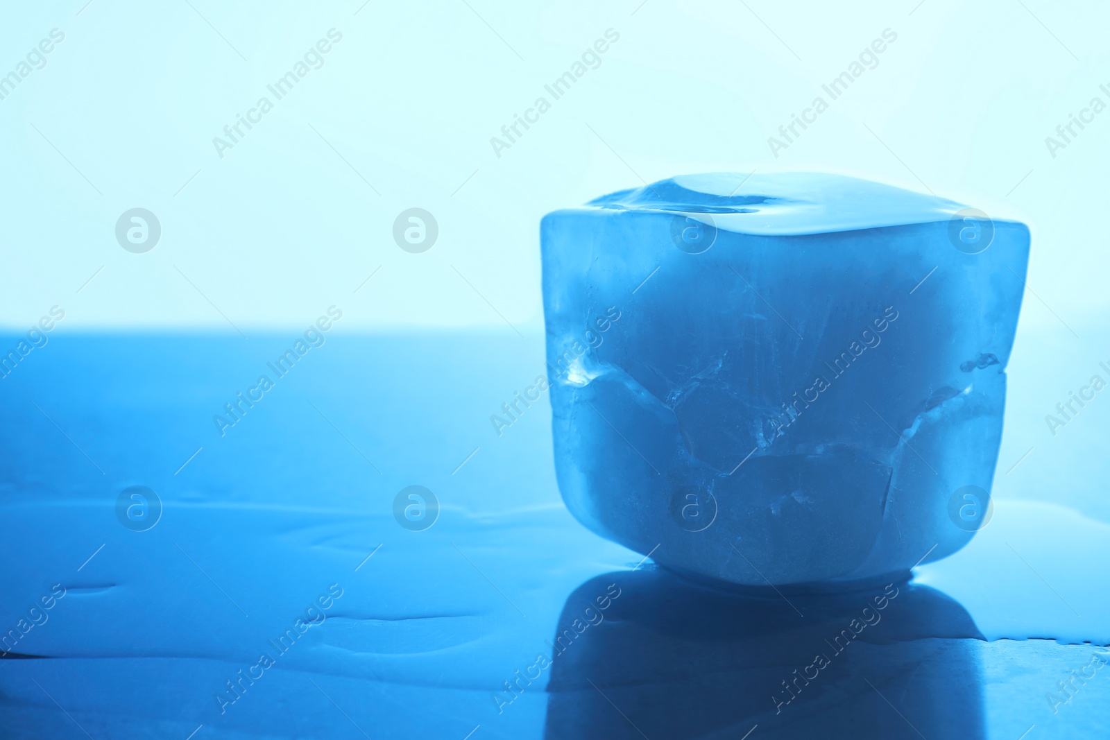 Photo of One crystal clear ice cube on light blue background, closeup and space for text. Color tone effect