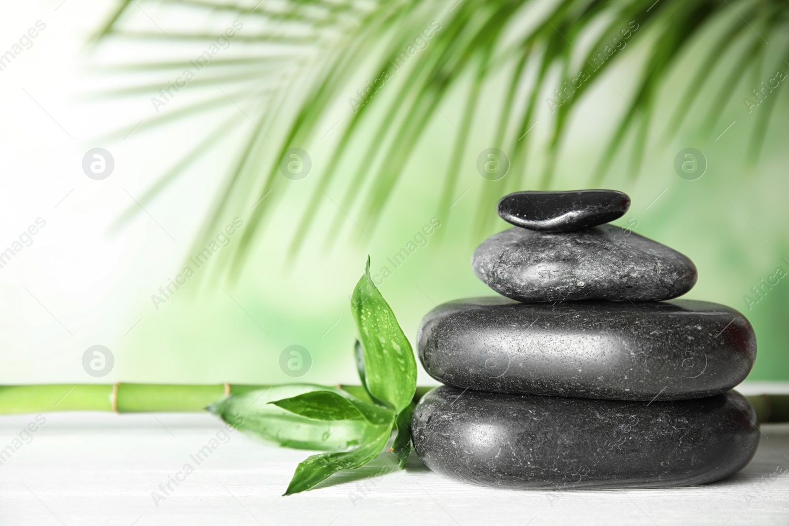 Photo of Spa stones pyramid and bamboo leaves on wooden table. Space for text