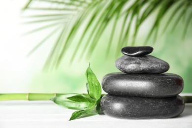 Photo of Spa stones pyramid and bamboo leaves on wooden table. Space for text