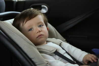 Photo of Cute little boy sitting in child safety seat inside car