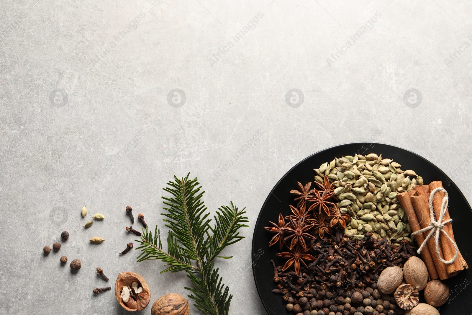 Photo of Different spices, nuts and fir branches on light gray textured table, flat lay. Space for text