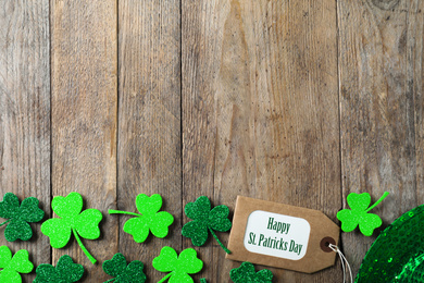 Clover leaves, tag and space for text on wooden table, flat lay. St. Patrick's Day celebration