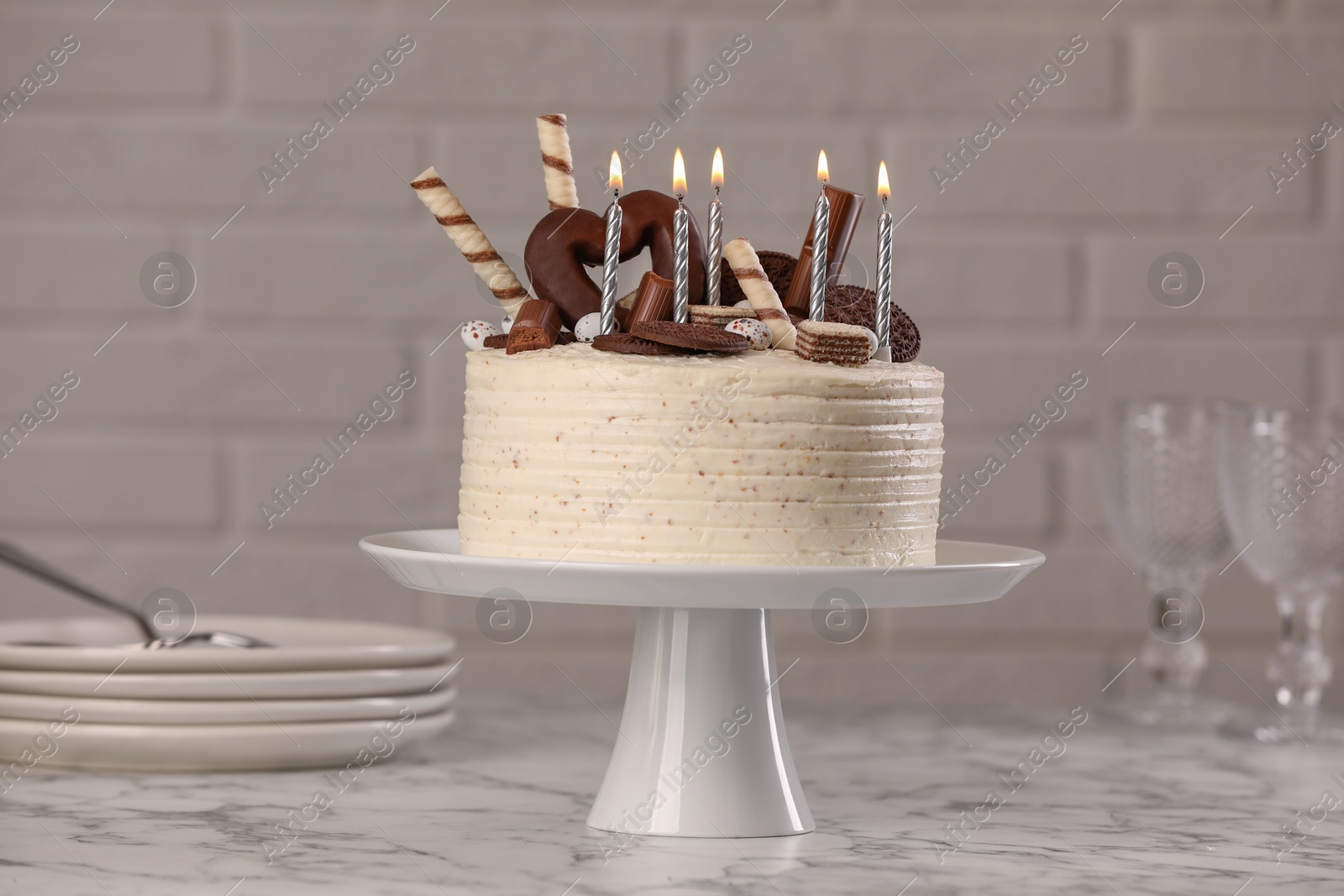 Photo of Delicious cake decorated with sweets and burning candles on white marble table