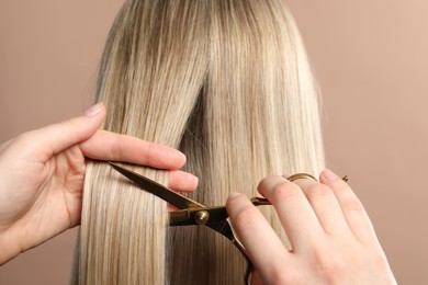 Photo of Hairdresser cutting client's hair with scissors on beige background, closeup