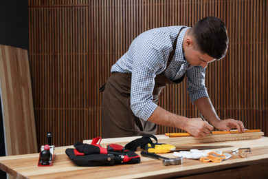 Carpenter marking length of wooden plank with pencil in workshop