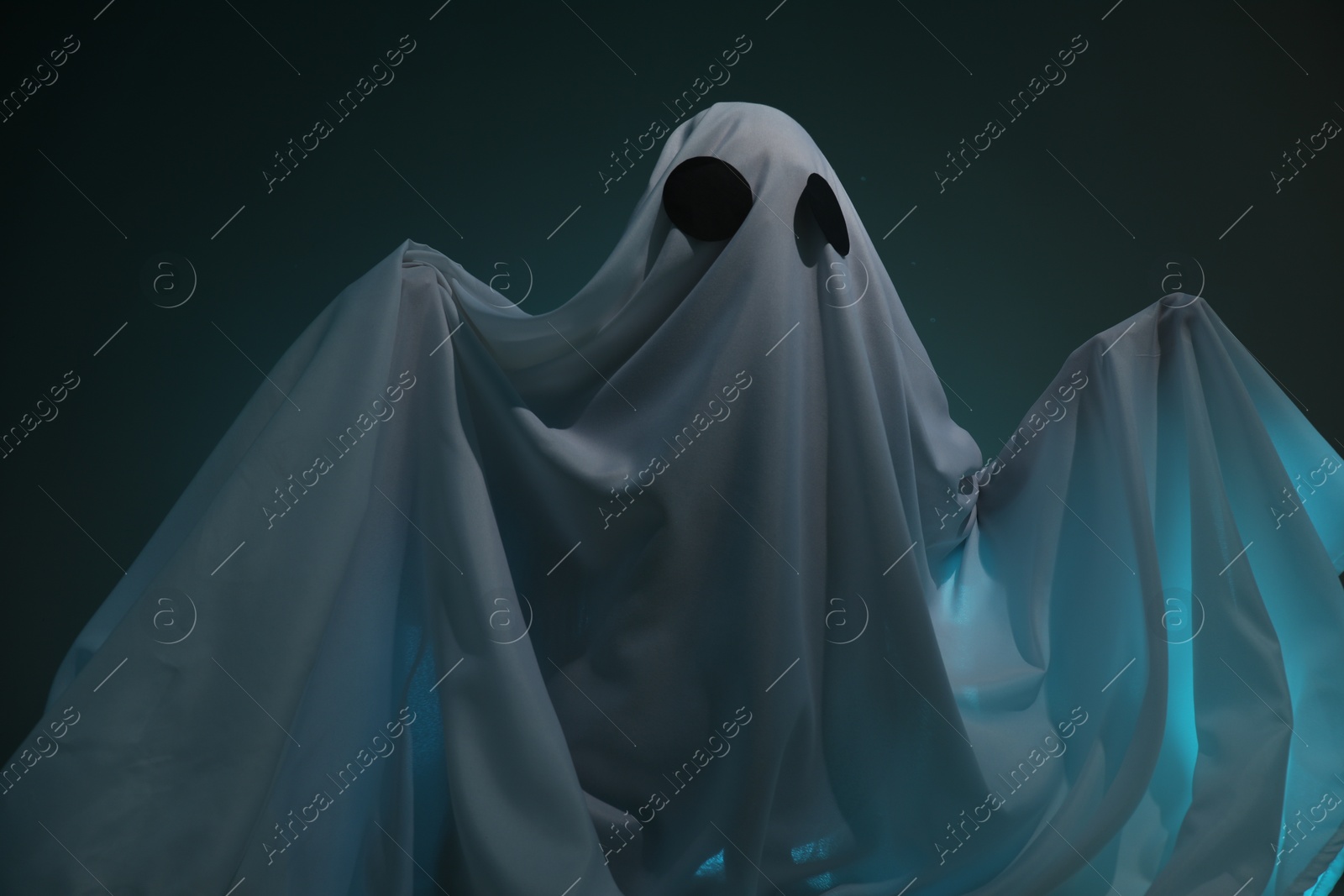 Photo of Creepy ghost. Woman covered with sheet on dark teal background