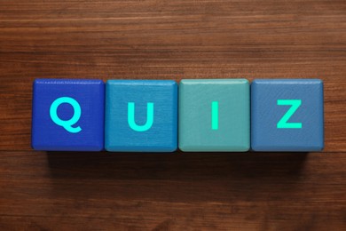 Photo of Blue cubes with word Quiz on wooden table, flat lay