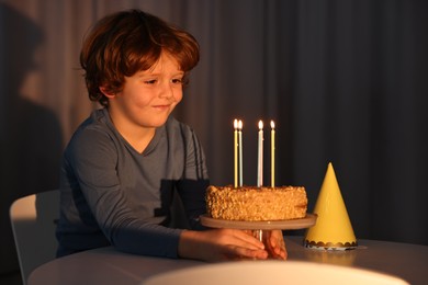 Cute boy with birthday cake at table indoors