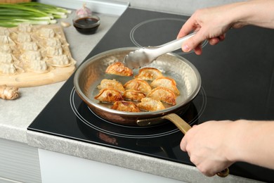 Photo of Woman cooking gyoza on frying pan with hot oil in kitchen, closeup