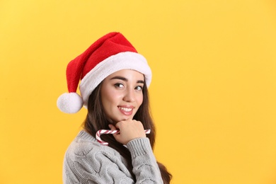 Photo of Beautiful woman in Santa Claus hat holding candy cane on yellow background