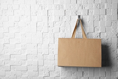 Photo of Paper shopping bag with comfortable handles hanging on white wall. Mockup for design