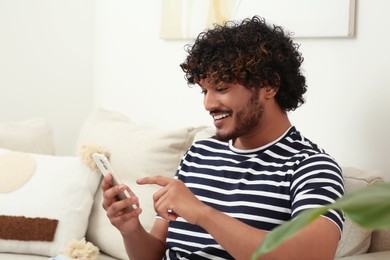 Handsome smiling man using smartphone in room, space for text