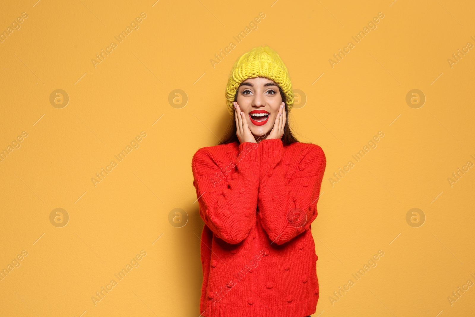 Photo of Young woman in warm sweater and knitted hat on color background. Celebrating Christmas