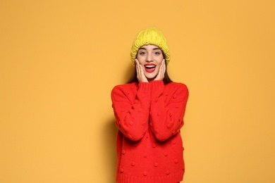 Young woman in warm sweater and knitted hat on color background. Celebrating Christmas