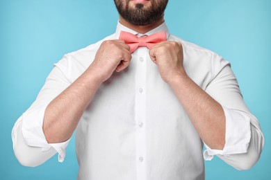 Photo of Man in shirt adjusting bow tie on light blue background, closeup