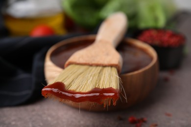 Photo of Marinade in bowl and basting brush on brown table, selective focus