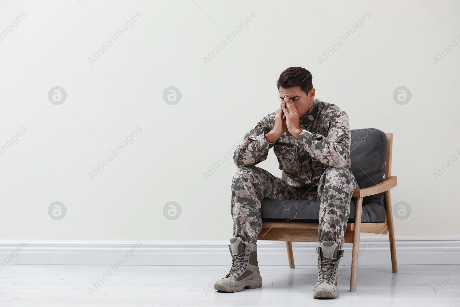 Photo of Stressed military officer sitting in armchair near white wall indoors. Space for text