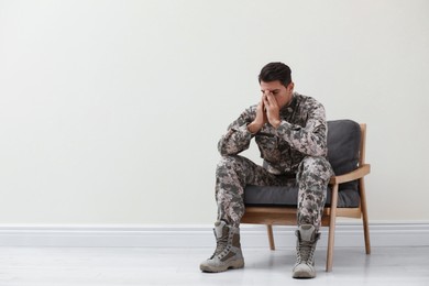 Photo of Stressed military officer sitting in armchair near white wall indoors. Space for text