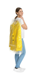 Young woman holding hanger with jacket in plastic bag on white background. Dry-cleaning service