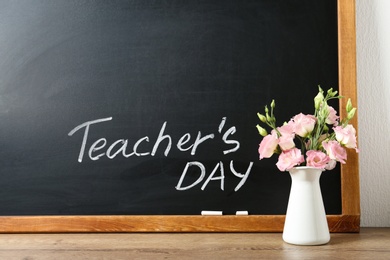 Photo of Blackboard with inscription TEACHER'S DAY and vase of flowers on wooden table