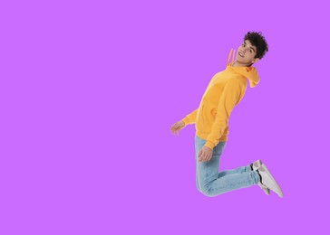 Teenage boy jumping on violet background, space for text