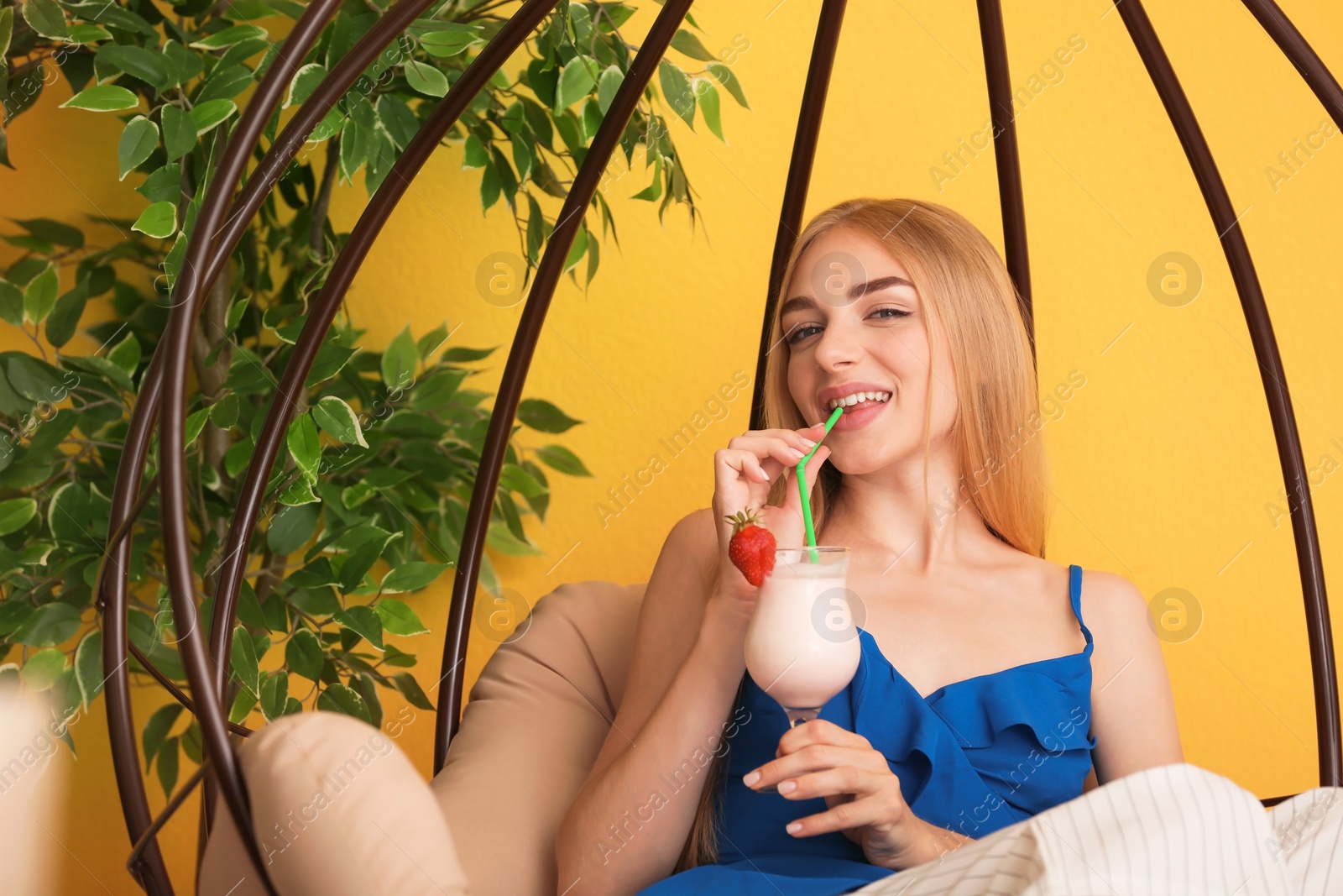 Photo of Young woman with glass of delicious milk shake in pendant chair indoors