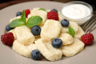 Photo of Tasty lazy dumplings with berries, sour cream and mint leaves on plate, closeup