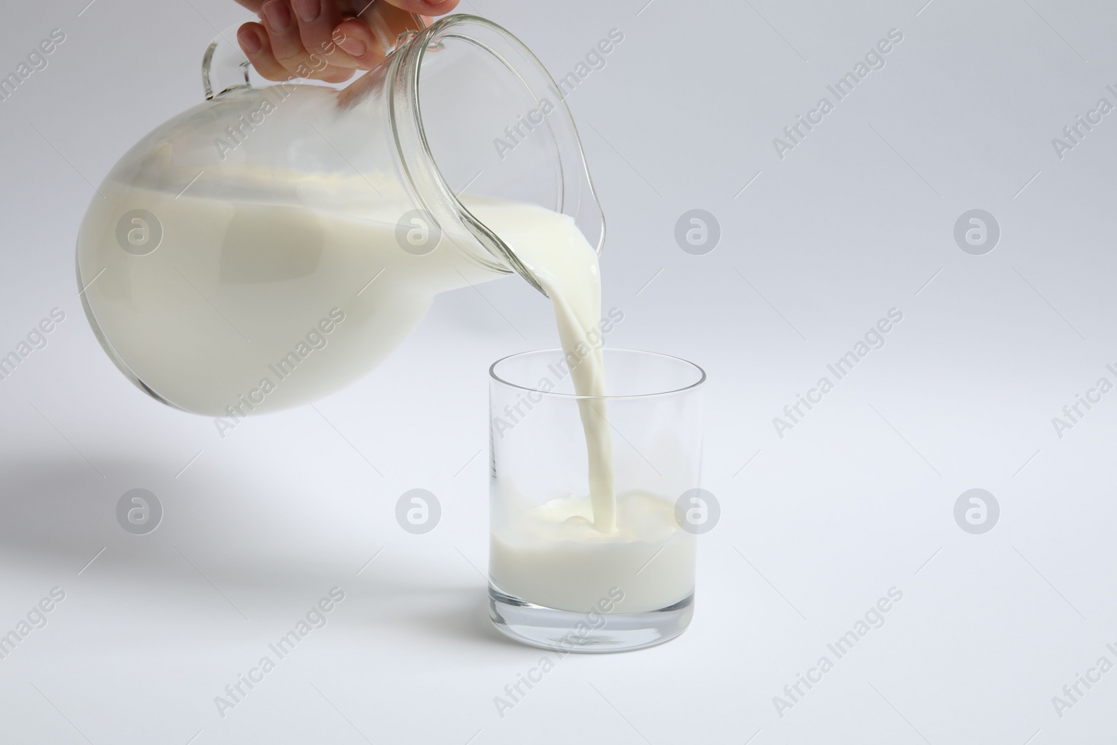 Photo of Woman pouring milk into glass on white background, closeup