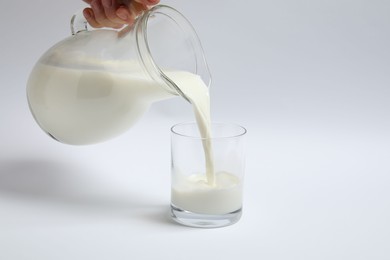 Woman pouring milk into glass on white background, closeup