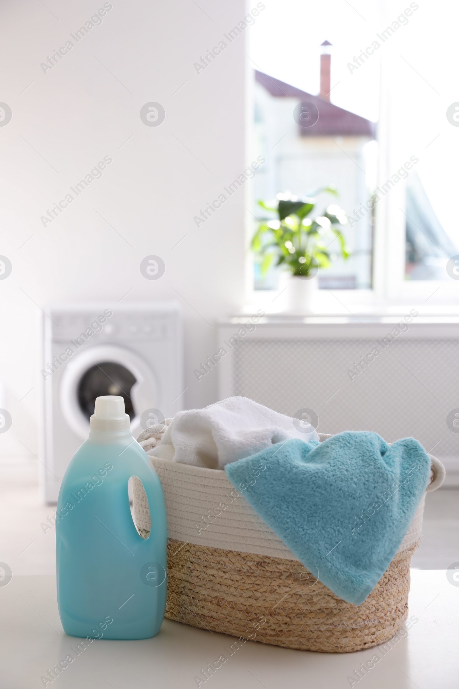Photo of Wicker basket with towels and detergent on white table indoors. Space for text