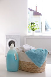 Photo of Wicker basket with towels and detergent on white table indoors. Space for text
