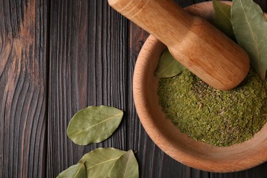 Photo of Mortar with whole and ground aromatic bay leaves on wooden table, flat lay