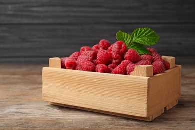 Photo of Crate of delicious fresh ripe raspberries with leaves on wooden table against dark background, space for text