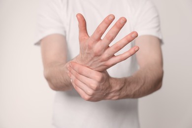 Man suffering from pain in his hand on light background, closeup. Arthritis symptoms
