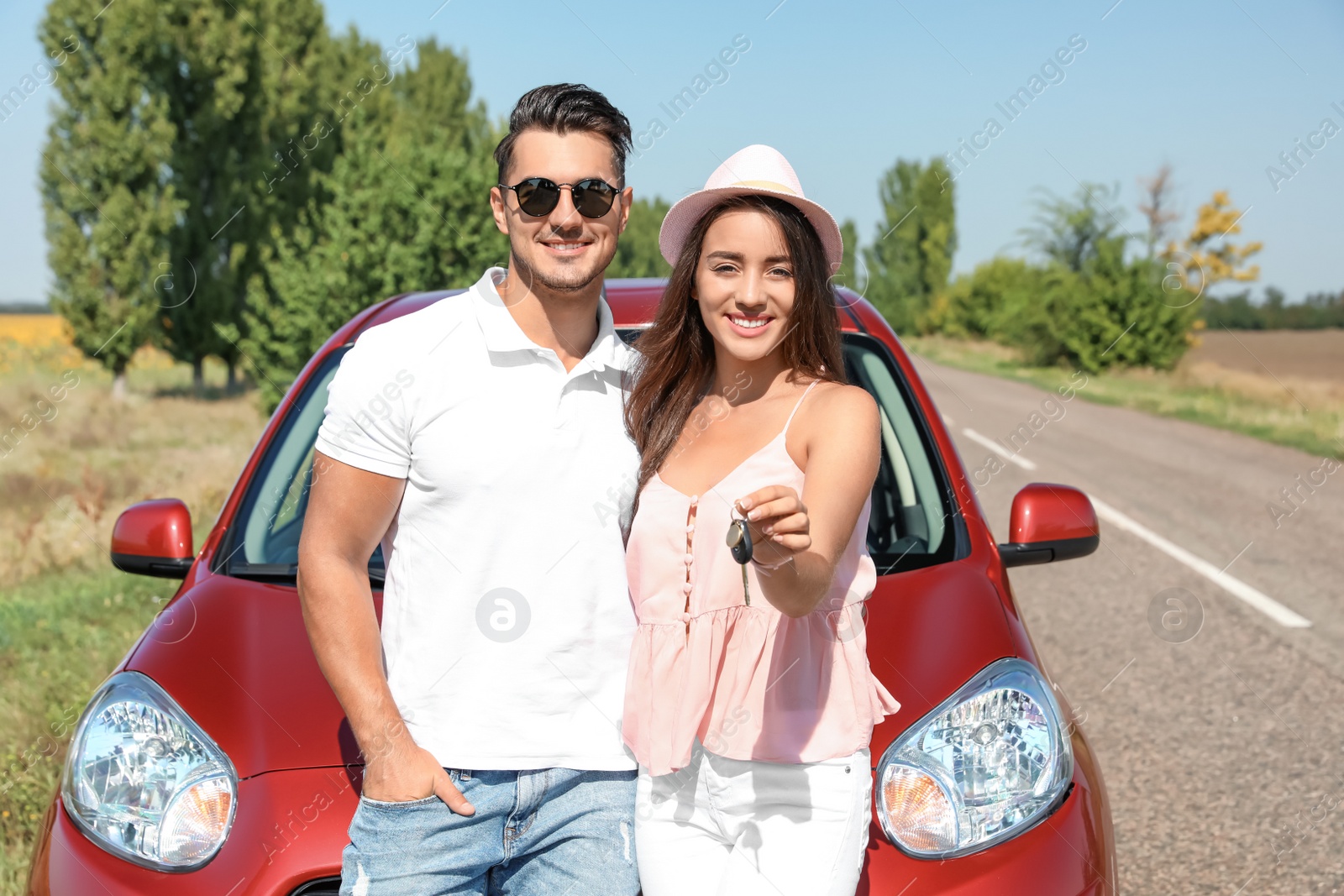 Photo of Happy young couple with key standing near new car on road