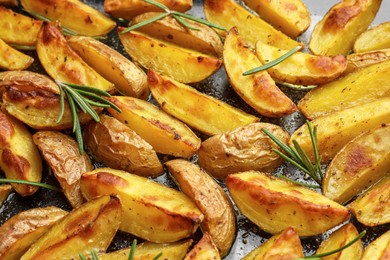 Photo of Delicious baked potatoes with rosemary on black surface, closeup