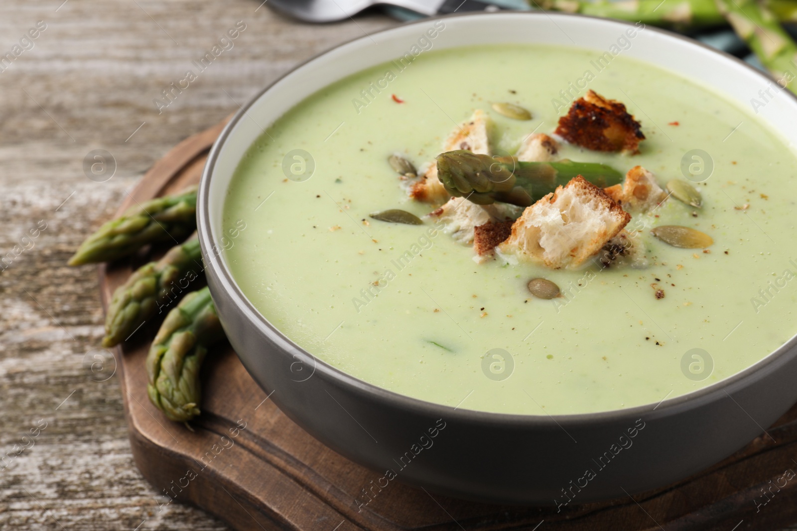 Photo of Bowl of delicious asparagus soup on wooden table, closeup