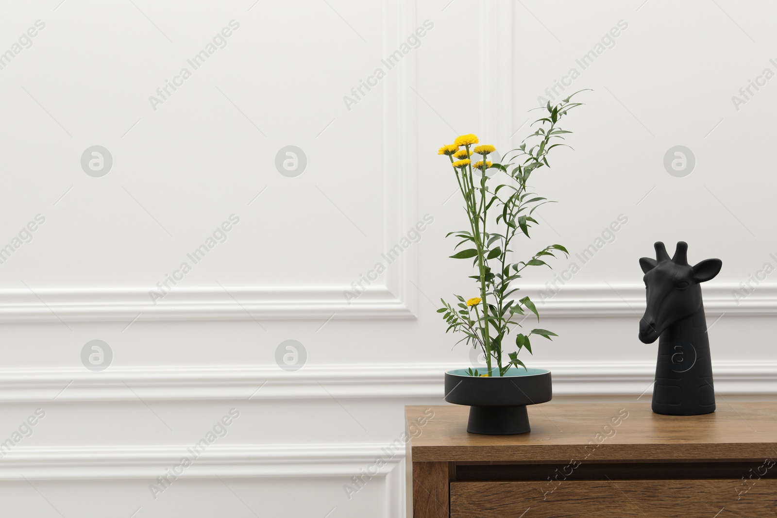 Photo of Stylish ikebana with beautiful yellow flowers, green branch and decor carrying cozy atmosphere at home, space for text