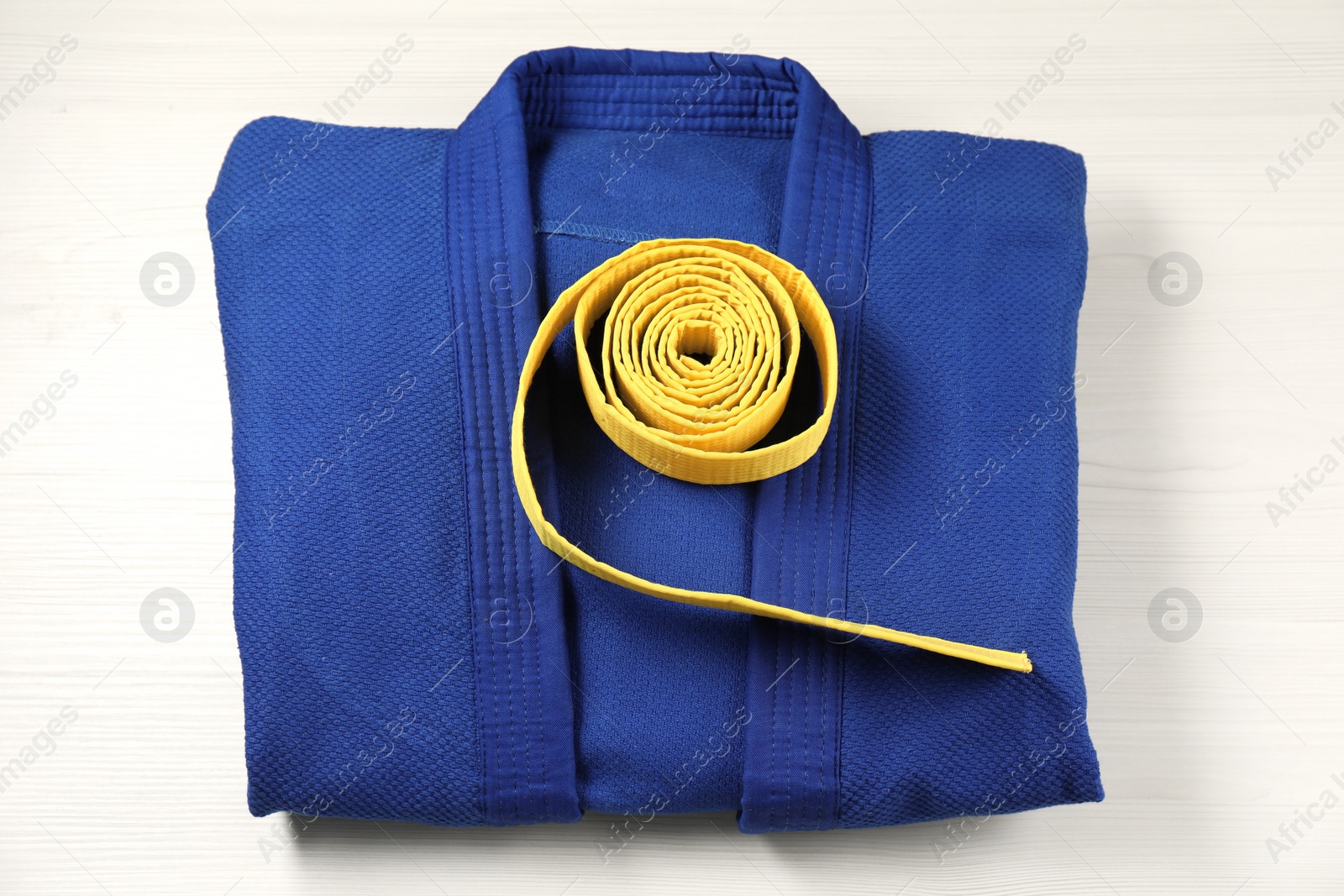 Photo of Yellow karate belt and blue kimono on wooden background, top view