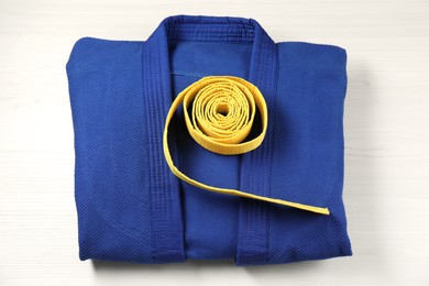 Yellow karate belt and blue kimono on wooden background, top view