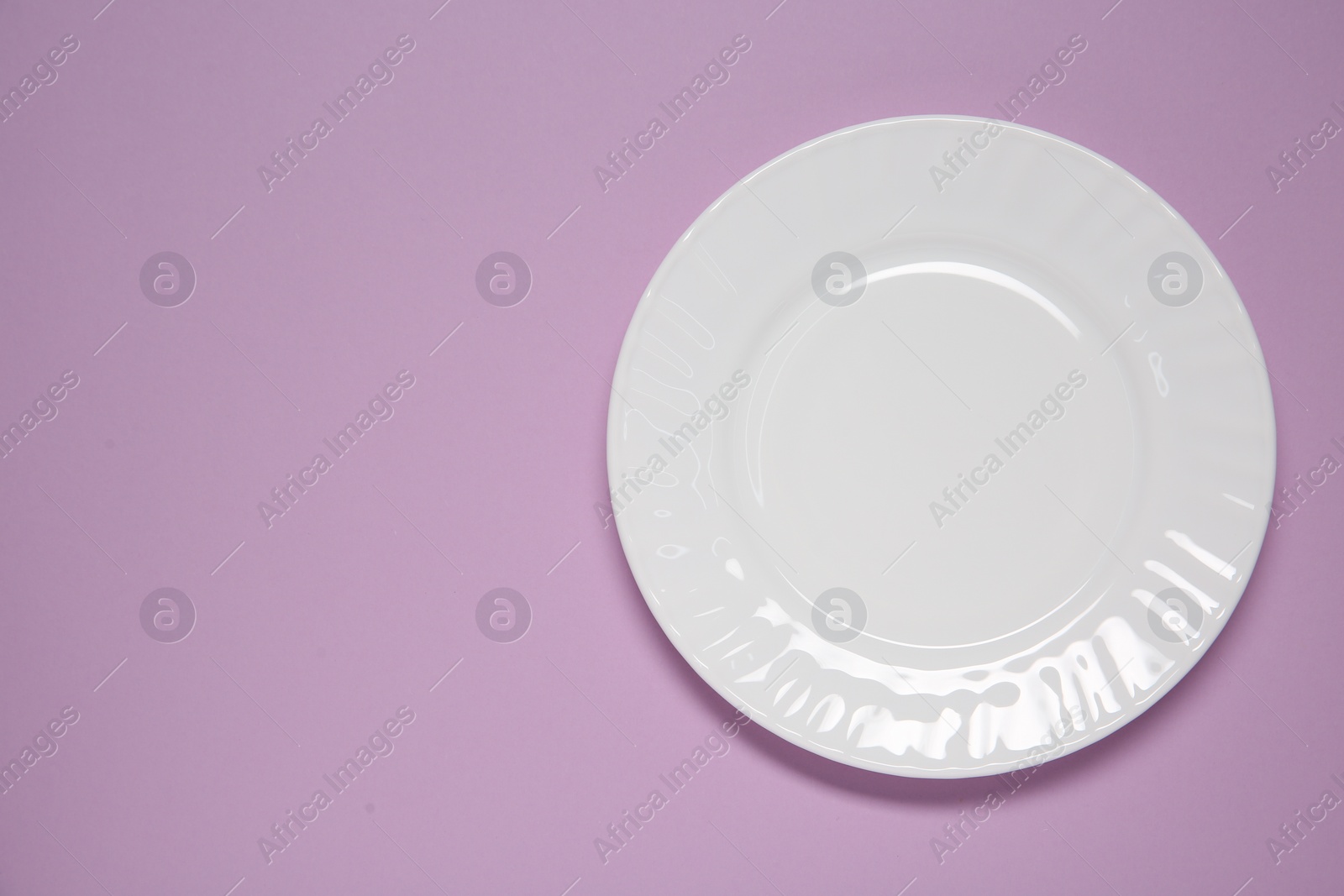 Photo of One white plate on violet background, top view. Space for text