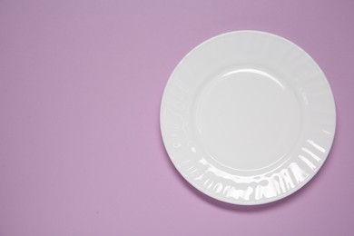 Photo of One white plate on violet background, top view. Space for text